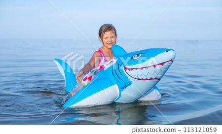 Happy girl swimming on an inflatable shark toy in the sea 113121059