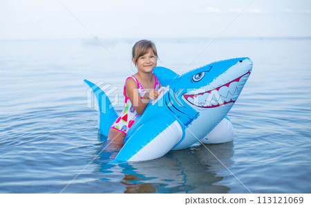 Happy girl swimming on an inflatable shark toy in the sea 113121069