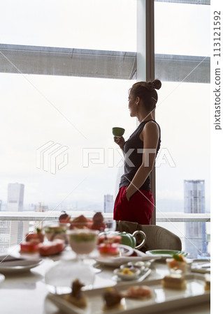 asian woman looking at view through window while enjoying room service 113121592