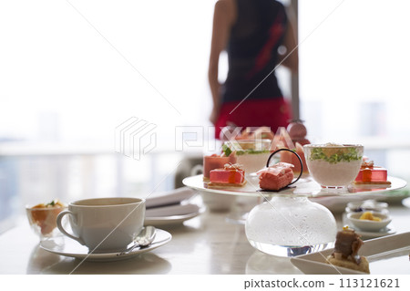 asian woman standing by window looking at city view with food on table in hotel room 113121621