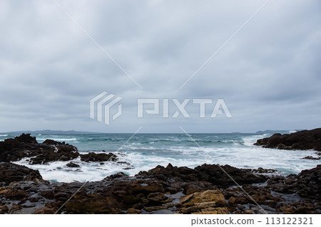 Surf on a rocky coast in front of the horizon under a cloudy sky. Tropical stormy ocean with waves crashing on the rocks. Stormy sea with stormy clouds and black lava rocks on the shore. Splashing Surf on a rocky coast in front of the horizon under a cloudy sky. Tropical stormy ocean with waves crashing on the rocks. Stormy sea with stormy clouds and black lava rocks on the shore. Splashing 113122321
