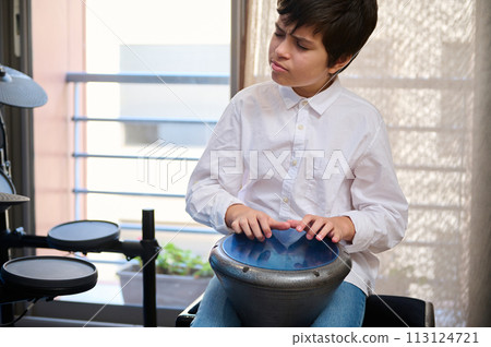 Teenage boy musician enjoying playing the African ethnic percussion musical instrument drum - djembe, bongo, tam tam. Happy teenager creating the rhythm of African music banging ethnic drum Teenage boy musician enjoying playing the African ethnic percussion musical instrument drum - djembe, bongo, tam tam. Happy teenager creating the rhythm of African music banging ethnic drum 113124721