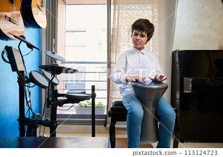 Caucasian handsome teenager, boy musician drummer banging drums tam tam bongo djembe, playing on traditional African ethnic percussion musical instrument Caucasian handsome teenager, boy musician drummer banging drums tam tam bongo djembe, playing on traditional African ethnic percussion musical instrument 113124723