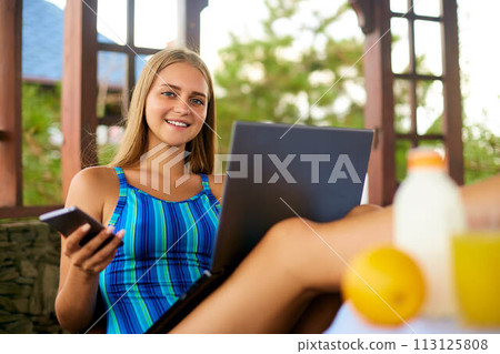 Freelancer woman sitting at garden house in tropical location and working with laptop getting her feet up on the table. Traveling Thailand with a computer and wi-fi internet. Telecommuting concept 113125808