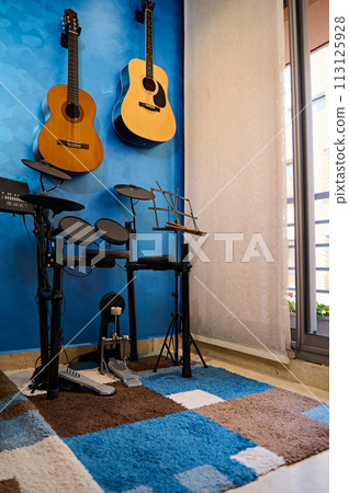 Modern interior of a music studio for home use. Acoustic nd electric guitars hanging on blue color wall and drum set. Hobbies and leisure. Musician's room for playing and learning music 113125928
