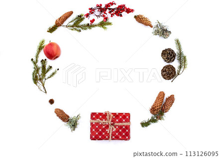 Christmas composition on isolated white background. New year wrapped gift, pine cones, thuja or fir branches, apple and red berries on snow. Top view, flat lay, copy space. Circular or rounded shape. 113126095