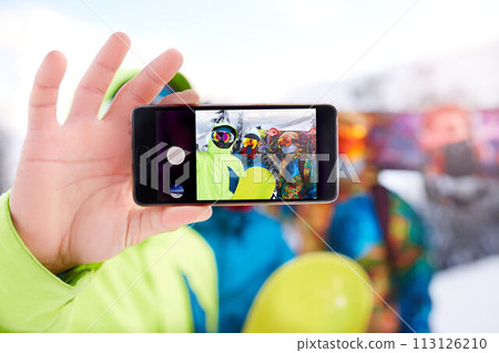 Smartphone screen with three snowboarders taking selfie at ski resort. Friends photographing for social network sharing with snowboards near forest wearing reflective goggles, colorful fashion clothes Smartphone screen with three snowboarders taking selfie at ski resort. Friends photographing for social network sharing with snowboards near forest wearing reflective goggles, colorful fashion clothes 113126210