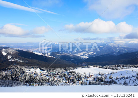 Panoramic view of Dragobrat ski resort from above. Mountain winter snowy landscape from ski slope. Wooden cottages and hotels in valley. Empty slope, no people. Product placement background for design Panoramic view of Dragobrat ski resort from above. Mountain winter snowy landscape from ski slope. Wooden cottages and hotels in valley. Empty slope, no people. Product placement background for design 113126241
