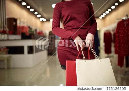Woman holding shopping bags while standing on store front in the mall background. Consumerism concept. Copyspace on bag. Woman holding shopping bags while standing on store front in the mall background. Consumerism concept. Copyspace on bag. 113126305