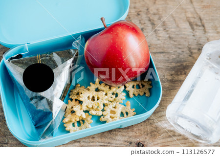 Asian student's lunchbox of onigiri,chips and apple with bottle of water,On wooden background 113126577