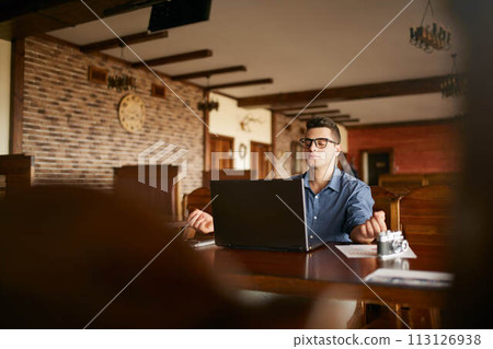 Businessman meditates sitting at table and laptop in office. Company leader practicing yoga during break at work for strength recovery and stress relief. Handsome man in glasses relaxing in cafe. 113126938