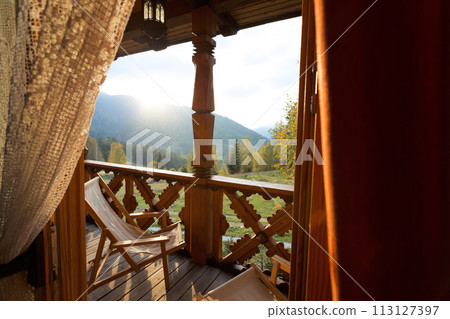 A deck chairs on balcony of the mountain spa resort apartment. Window view at wooden terrace with autumn forest background at country house. No people 113127397