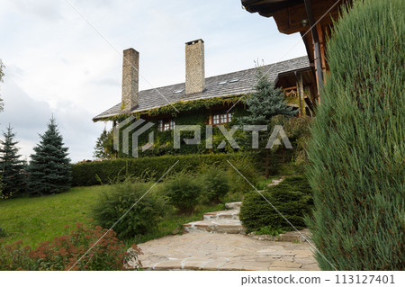 Vintage log wooden house covered by green ivy. Rural country house with chimney, cottage, covered with ivy, herbage. Eco floristic facade design. Vintage log wooden house covered by green ivy. Rural country house with chimney, cottage, covered with ivy, herbage. Eco floristic facade design. 113127401