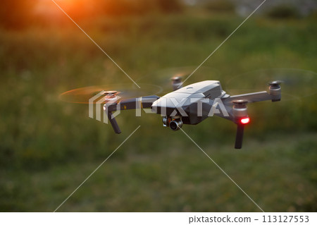 Small compact quadcopter flies in the air on sunset. Drone hovers and stays stable. 113127553