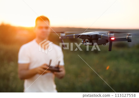 Drone hovers in front of man with remote controller in his hands. Quadcopter flies near pilot. Guy taking aerial photos and videos from above Drone hovers in front of man with remote controller in his hands. Quadcopter flies near pilot. Guy taking aerial photos and videos from above 113127558