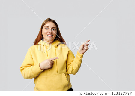 Pretty cheerful woman in casual clothes gesturing with fingers and showing away isolated over gray background, studio portrait. Human emotions, facial expression and symbols concept. 113127787