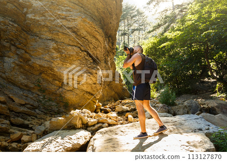Bearded photographer man trekking among forest and mountains and taking pictures with dslr camera. Horizontal shape, copy space Bearded photographer man trekking among forest and mountains and taking pictures with dslr camera. Horizontal shape, copy space 113127870