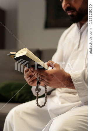 Vertical selective focus shot of bearded Middle Eastern man holding misbaha reading Quran book Vertical selective focus shot of bearded Middle Eastern man holding misbaha reading Quran book 113128030