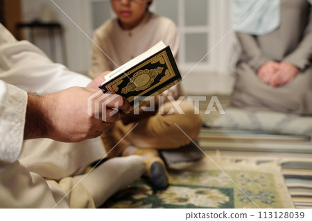 Selective focus closeup of unrecognizable Muslim man reading Quran surah at family gathering at home, copy space Selective focus closeup of unrecognizable Muslim man reading Quran surah at family gathering at home, copy space 113128039