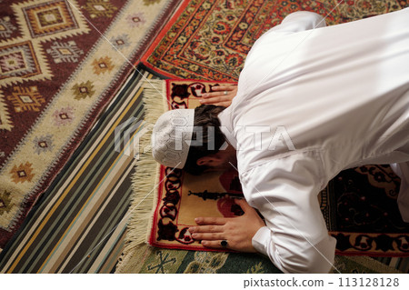 High angle view of unrecognizable young Muslim man wearing white clothes doing sadjah on prayer rug during namaz, copy space 113128128