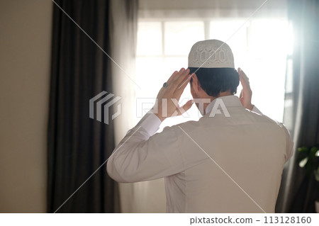 Rear view of unrecognizable young Muslim man wearing white thobe and taqiyah praying salah, copy space Rear view of unrecognizable young Muslim man wearing white thobe and taqiyah praying salah, copy space 113128160