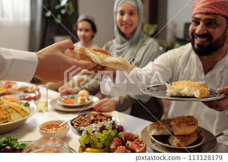 Selective focus shot of cheerful Muslim family sharing bread while having festive dinner on Eid Al-Fitr 113128179