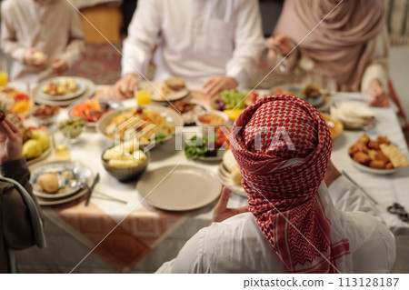 High angle view selective focus shot of unrecognizable Muslim man wearing keffiyeh having festive dinner with his family, copy space 113128187