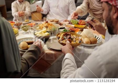 Selective focus over-shoulder shot of unrecognizable Muslim family sitting at festive table having dinner on Eid Al-Fitr 113128194