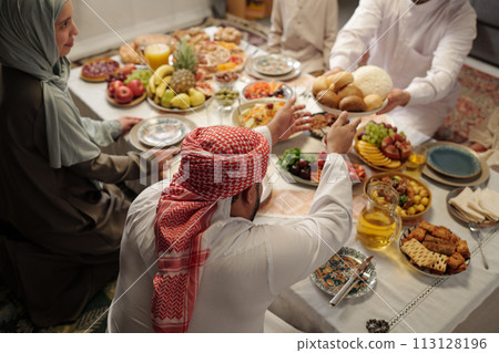 High angle view of young Muslim man sharing food with his family at festive dinner on Uraza Bayram 113128196