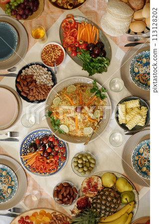 Vertical flat lay no people shot of pilaf, vegetables, fruits and snacks on festive table on Uraza Bayram day 113128202