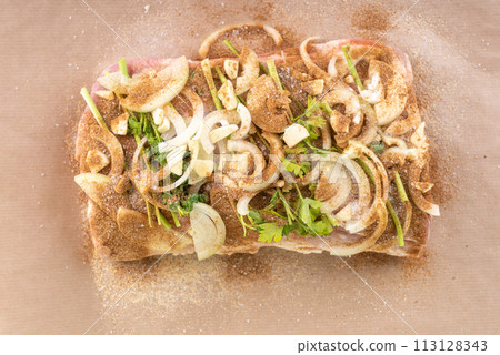 Top view of meat sprinkled with spices, onion and garlic pieces, ready for baking. Top view of meat sprinkled with spices, onion and garlic pieces, ready for baking. 113128343