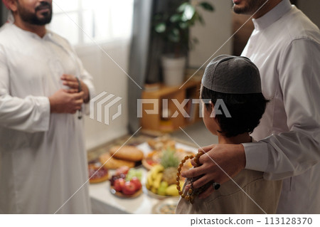 Selective focus shot of proud Muslim father and his son talking to male relative at family gathering on Eid Al-Fitr, copy space 113128370