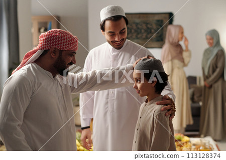 Cheerful bearded Middle Eastern man patting his nephew on head at family gathering on Uraza Bayram day 113128374