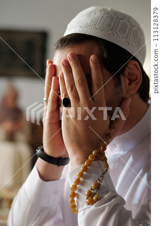 Vertical closeup of unrecognizable muslim man wearing taqiyah holding mishaba praying salah 113128379