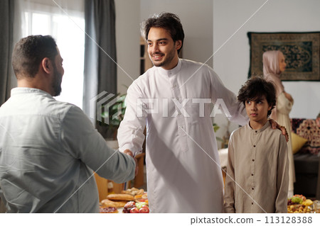 Medium shot of young Muslim man and his son wearing thobes greeting male relative on Eid al-Fitr Medium shot of young Muslim man and his son wearing thobes greeting male relative on Eid al-Fitr 113128388