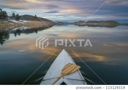 bow of expedition canoe with a wooden paddle at calm winter dusk over mountain lake - Horsetooth Reservoir bow of expedition canoe with a wooden paddle at calm winter dusk over mountain lake - Horsetooth Reservoir 113129319