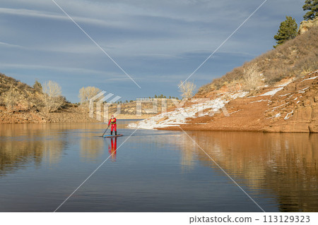 male paddler in red drysuit is paddling a stand up paddleboard on mountain lake in Colorado, winter scenery male paddler in red drysuit is paddling a stand up paddleboard on mountain lake in Colorado, winter scenery 113129323