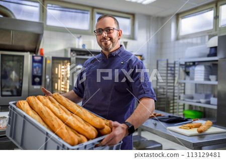 Smiling man employee holding baguettes at bakery Smiling man employee holding baguettes at bakery 113129481
