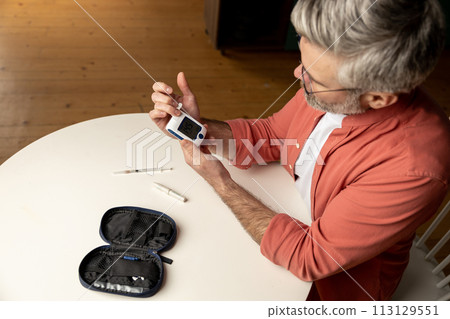 Middle aged man with glucometer checking blood sugar level at home 113129551