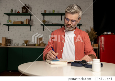 Diabetic man checking level of sugar in blood with glucometer takes notes with indicators in notepad Diabetic man checking level of sugar in blood with glucometer takes notes with indicators in notepad 113129561