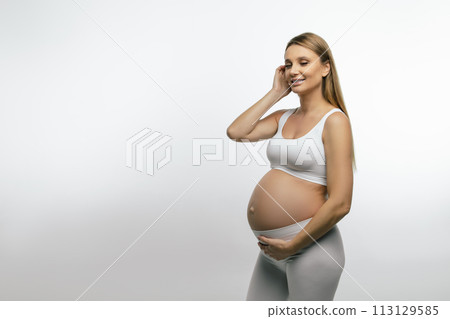 Blonde pregnant woman in white clothes looking thoughtful 113129585