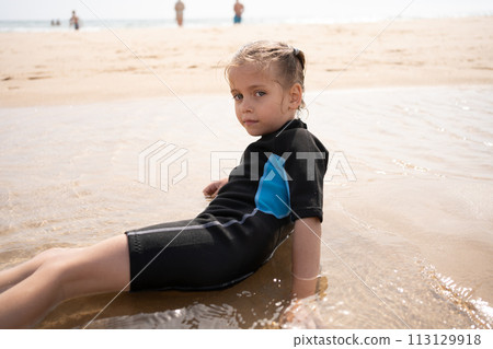 Little girl surfer in wetsuit lies ocean beach 113129918