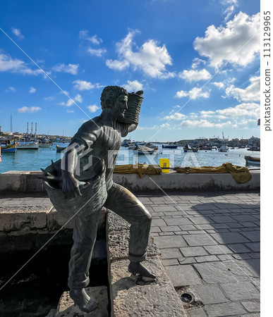 A wonderful monument on the shore of Marsaxlokk, Malta: a young son and daughter meet a father who is carrying two wicker baskets full of caught fish. A wonderful monument on the shore of Marsaxlokk, Malta: a young son and daughter meet a father who is carrying two wicker baskets full of caught fish. 113129965
