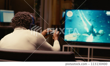 African american gamer excited after winning game playing arcade space shooter on ultrawide TV. Man spending time in apartment on gaming system, happy to finally solve singleplayer videogame mission 113130400