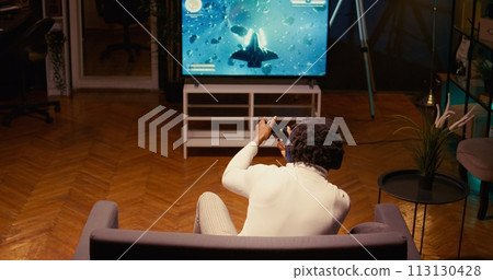 Gamer shooting foes, trying to defeat them in classic arcade space shooter videogame on smart TV. Man spamming buttons on controller to complete missions in singleplayer game 113130428