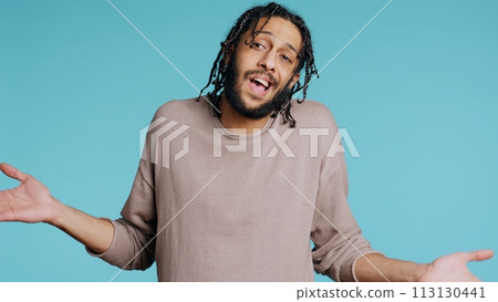 Uncaring Middle Eastern man shrugging shoulders, showing indifference and apathy. Careless BIPOC person doing nonchalant indifferent hand gesturing, isolated over studio background, camera B 113130441