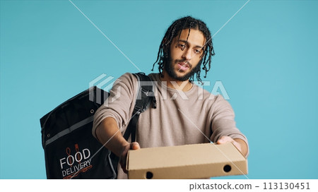Portrait of BIPOC courier delivering pizza order to client. Delivery part time worker using thermal backpack to store food and bring it to customer, isolated over studio background, camera A Portrait of BIPOC courier delivering pizza order to client. Delivery part time worker using thermal backpack to store food and bring it to customer, isolated over studio background, camera A 113130451
