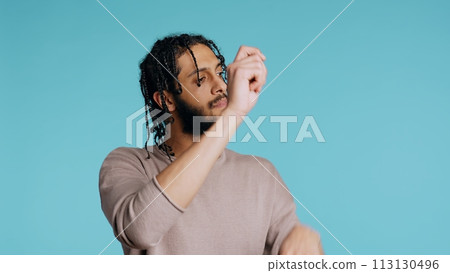 Middle Eastern conductor performing classical music concert following imaginary sheet music. Man doing delicate swinging hand motions, pretending to conduct orchestra, studio background, camera B 113130496