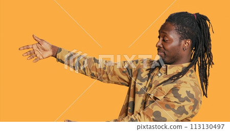 African american guy does advertisement for web marketing, showing thumbs up sign and presenting something to the left. Male model creating ad for promotional campaign. Handheld shot. 113130497