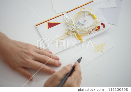 Hand of a middle-aged woman writing her name with a brush on a celebratory noshi bag 113130898